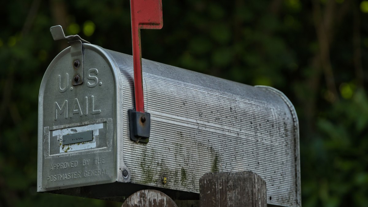 A weathered aluminum U.S. Mail curbside mailbox with the red flag raised.